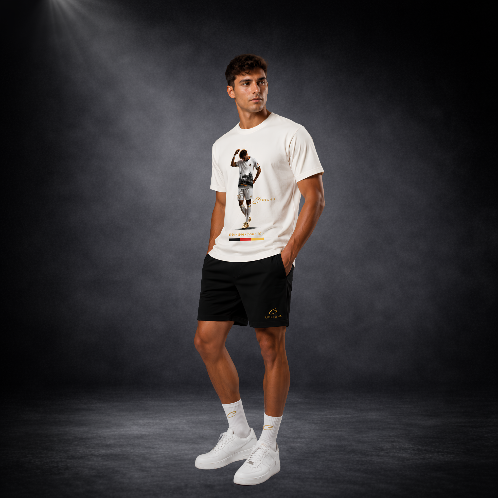Ganzkörperaufnahme eines jungen männlichen Models in modernem Deutschland Fußball-Lifestyle-Outfit von CERTANU vor dunklem Studiohintergrund mit Spotlight-Beleuchtung. Das Model trägt ein cremeweißes Premium-T-Shirt mit exklusivem Fußballspieler-Design, goldenen Fußballschuhen, der Nummer 10 und integrierten Berliner Wahrzeichen. Unter dem Motiv sind die Weltmeisterjahre 1954, 1974, 1990 und 2014 sowie die deutschen Nationalfarben Schwarz, Rot und Gold dargestellt. Kombiniert wird das Shirt mit schwarzen CE