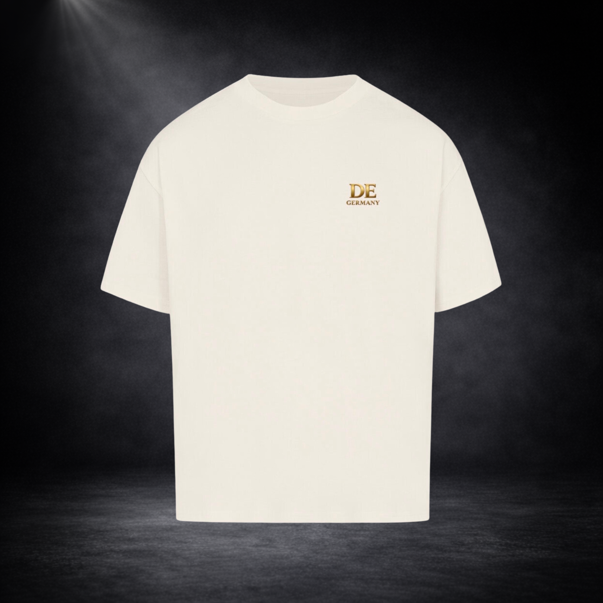 Beigefarbenes Oversized T-Shirt mit kleinem goldenen „DE Germany“-Print auf der Brust, präsentiert vor dunklem Studio-Hintergrund im minimalistischen Premium-Stil