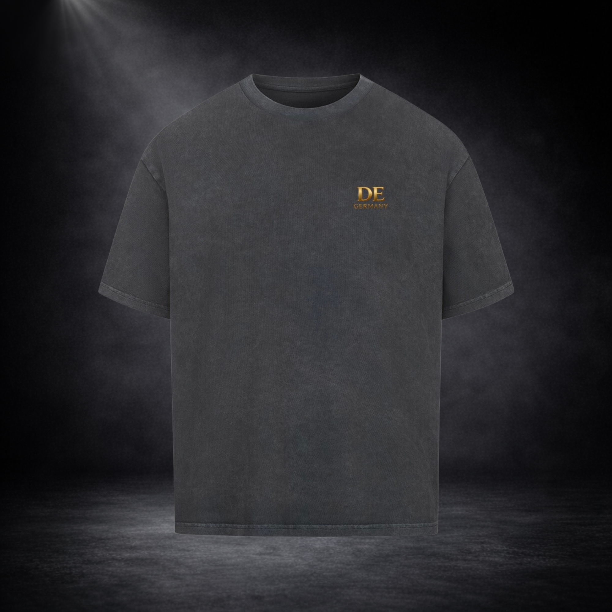 Dunkelgraues Oversized T-Shirt mit kleinem goldenen „DE Germany“-Print auf der Brust, präsentiert vor dunklem Studio-Hintergrund im minimalistischen Premium-Look