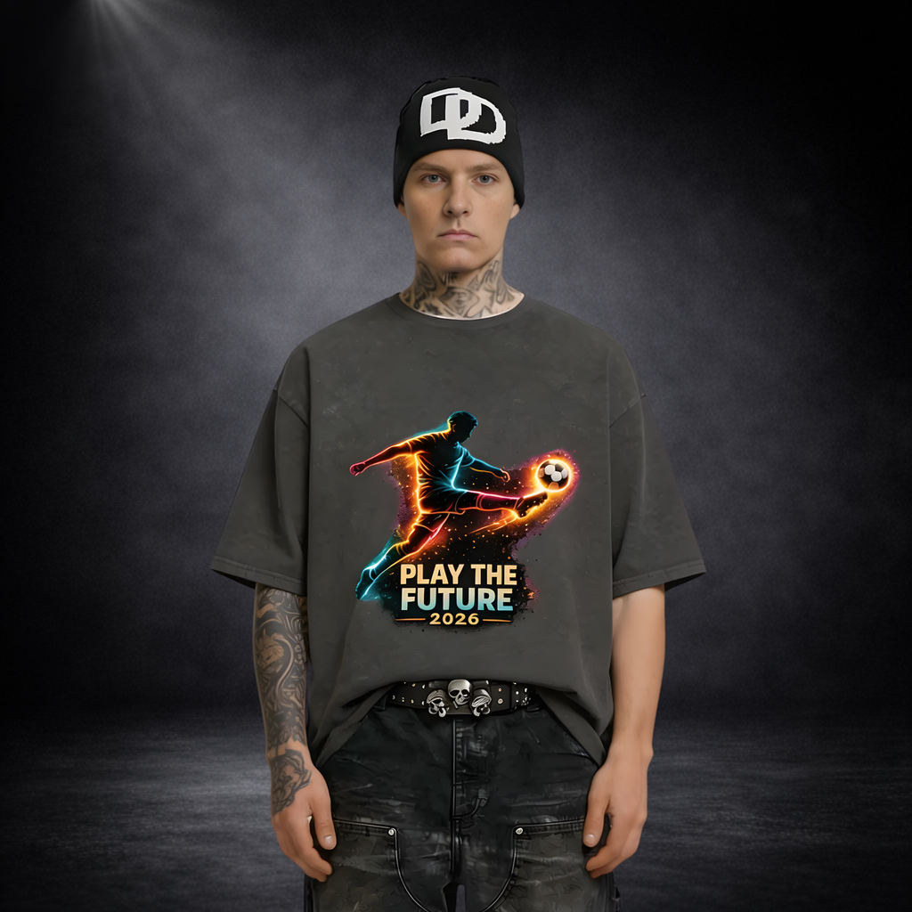 Männliches Model mit schwarzer Mütze und dunklem T-Shirt mit leuchtendem Fußballspieler-Print „Play the Future 2026“, vor dunklem Studio-Hintergrund