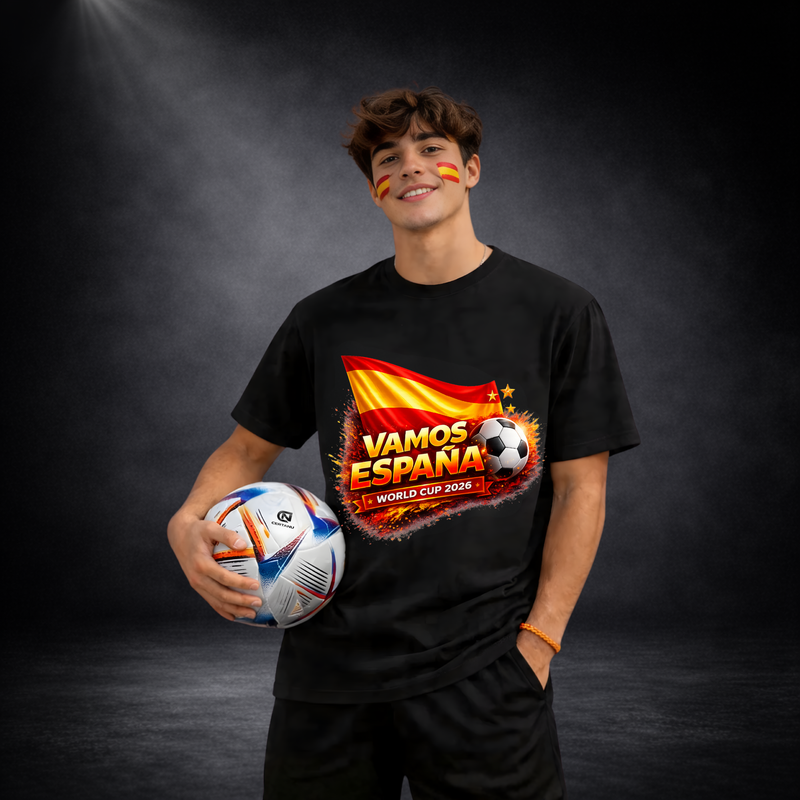 Junger Mann mit schwarzem T-Shirt und Spanien-Design („VAMOS ESPAÑA – WORLD CUP 2026“), hält einen Fußball in der Hand, mit Spanien-Fanbemalung im Gesicht vor dunklem Studio-Hintergrund