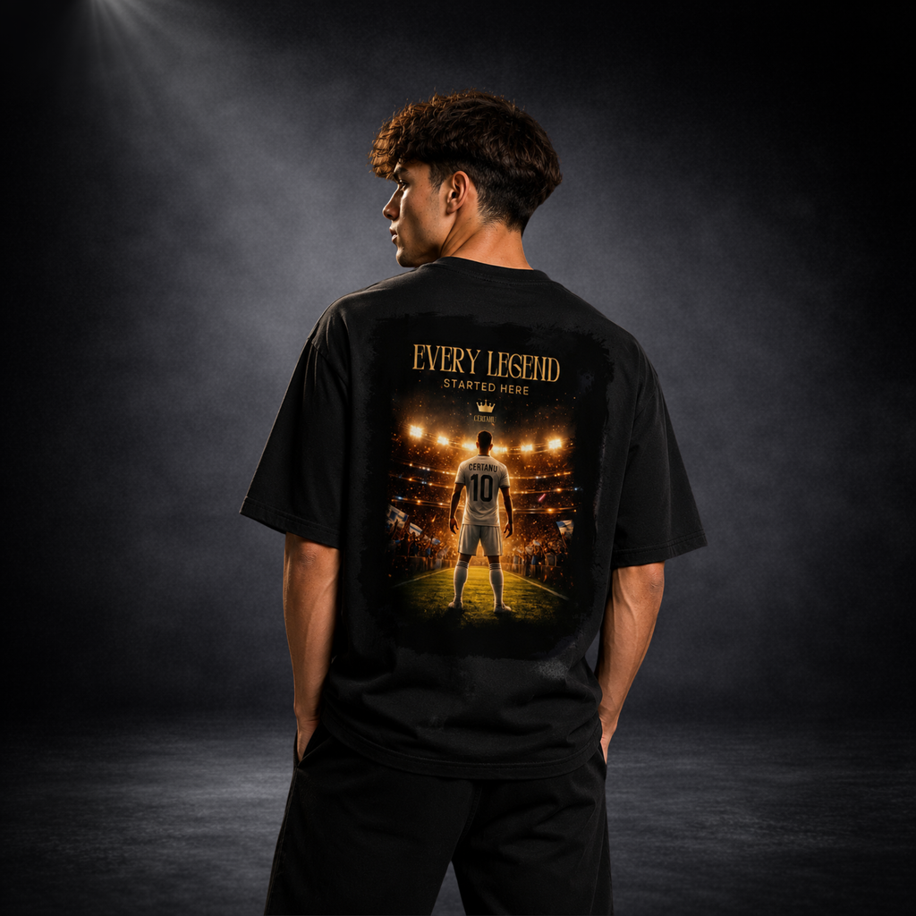 Junger Mann trägt ein schwarzes Oversized T-Shirt von CERTANU und präsentiert die Rückseite des Designs in einer hochwertigen Studioaufnahme mit dunklem Hintergrund und dramatischer Beleuchtung. Das große Rückenmotiv zeigt einen Fußballspieler mit der Nummer 10, der unter Flutlicht in ein ausverkauftes Stadion blickt. Darüber steht der inspirierende Schriftzug „EVERY LEGEND STARTED HERE“. Die Szene symbolisiert den Weg vom Traum zum Erfolg im Fußball und vermittelt Motivation, Leidenschaft und Ehrgeiz. Das 