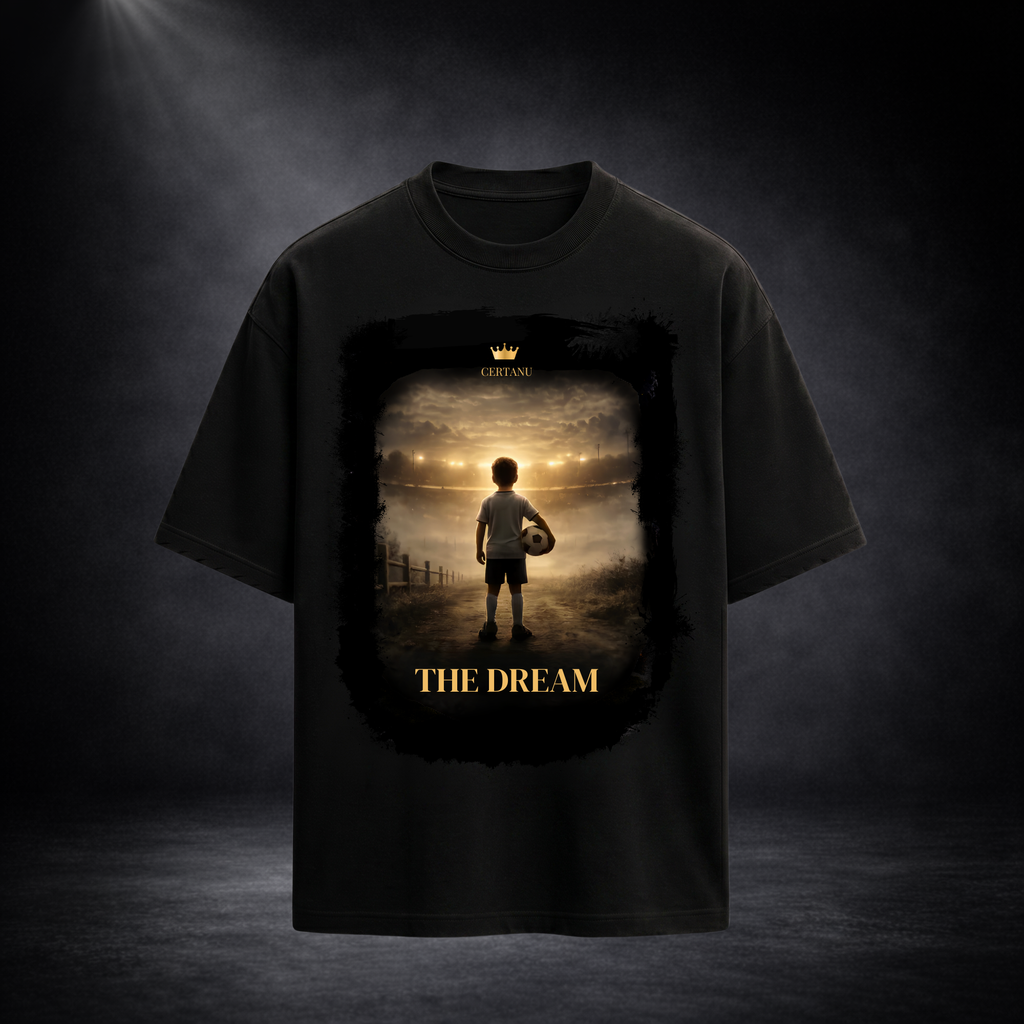 Schwarzes Oversized T-Shirt von CERTANU mit großem Frontprint vor dunklem Premium-Studiohintergrund. Das Design zeigt einen jungen Fußballspieler mit Ball, der auf ein hell erleuchtetes Stadion in der Ferne blickt. Warme Gold- und Lichttöne erzeugen eine emotionale Atmosphäre und symbolisieren den Traum vom Profifußball. Unter dem Motiv steht der Schriftzug „THE DREAM“ in goldener Typografie. Das hochwertige Fußball-Design vermittelt Motivation, Leidenschaft, Ehrgeiz und den Weg vom Nachwuchsspieler zur Leg