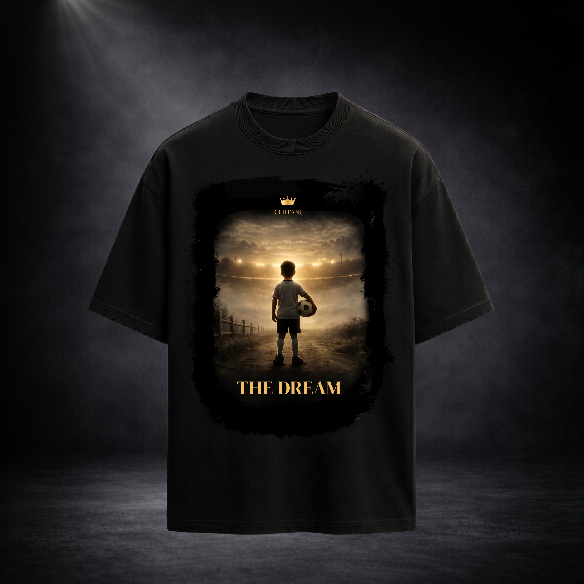 Schwarzes Oversized T-Shirt von CERTANU mit großem Frontprint vor dunklem Premium-Studiohintergrund. Das Design zeigt einen jungen Fußballspieler mit Ball, der auf ein hell erleuchtetes Stadion in der Ferne blickt. Warme Gold- und Lichttöne erzeugen eine emotionale Atmosphäre und symbolisieren den Traum vom Profifußball. Unter dem Motiv steht der Schriftzug „THE DREAM“ in goldener Typografie. Das hochwertige Fußball-Design vermittelt Motivation, Leidenschaft, Ehrgeiz und den Weg vom Nachwuchsspieler zur Leg