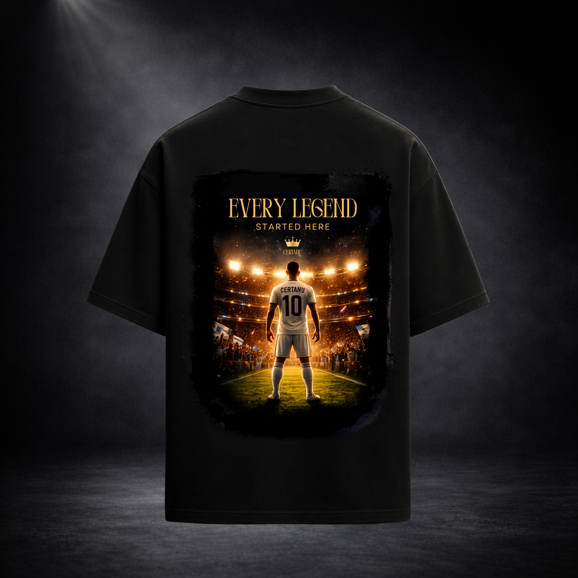 Rückseite eines schwarzen Oversized T-Shirts von CERTANU vor dunklem Premium-Studiohintergrund. Das großflächige Rückenmotiv zeigt einen Fußballspieler mit der Nummer 10, der unter hellen Stadionlichtern auf dem Spielfeld steht und auf eine jubelnde Menschenmenge blickt. Über dem Motiv steht der goldene Schriftzug „EVERY LEGEND STARTED HERE“. Das Design symbolisiert den Weg vom Nachwuchsspieler zur Fußballlegende, Leidenschaft, Ehrgeiz und große Träume. Warme Goldtöne, dramatische Beleuchtung und eine hochw