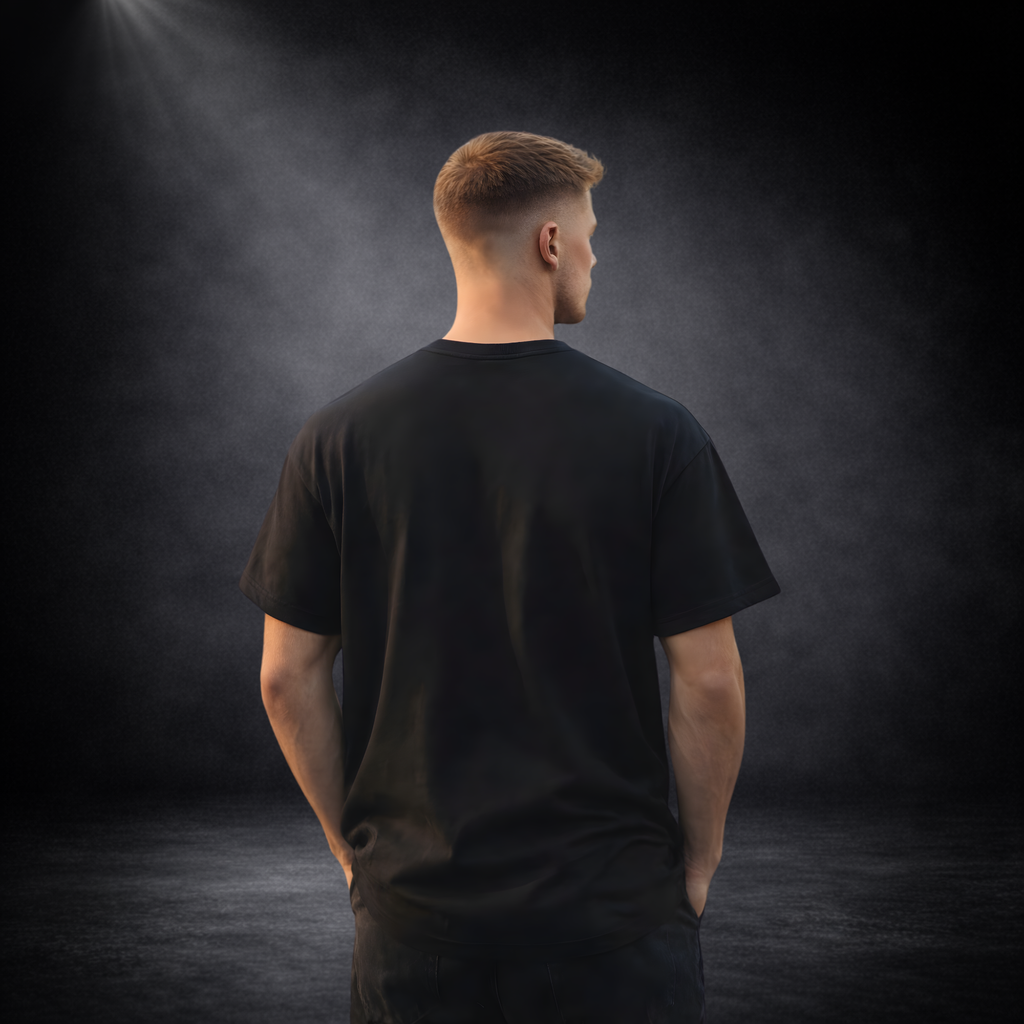Rückansicht eines männlichen Models in schwarzem T-Shirt ohne Aufdruck, vor dunklem Studio-Hintergrund mit weichem Licht von oben