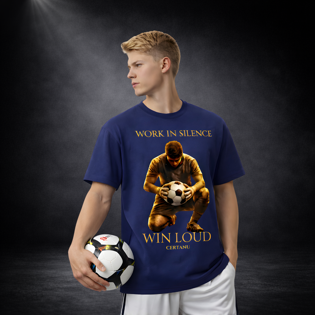Junger Mann im Profil trägt blaues T-Shirt mit großem Fußball-Motiv und goldener Schrift „Work in Silence – Win Loud“, hält einen Fußball in der Hand, vor dunklem Studio-Hintergrund
